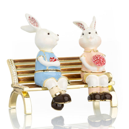 2 bunnies in love sitting on a bench, valentine flowers and chocolates by Keren Kopal