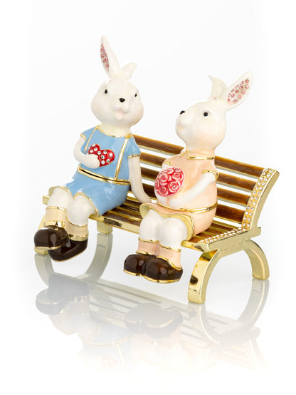 2 bunnies in love sitting on a bench, valentine flowers and chocolates by Keren Kopal