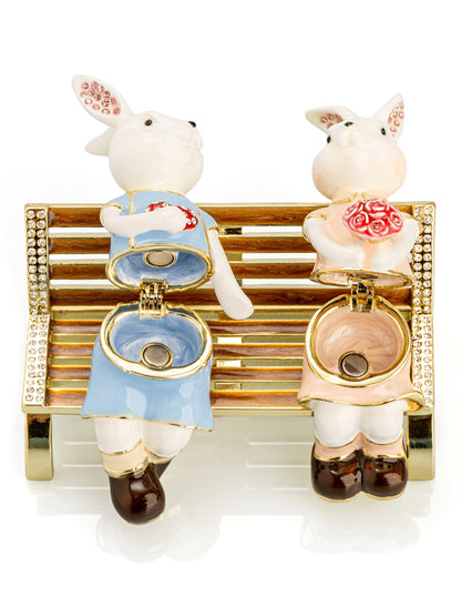 2 bunnies in love sitting on a bench, valentine flowers and chocolates by Keren Kopal